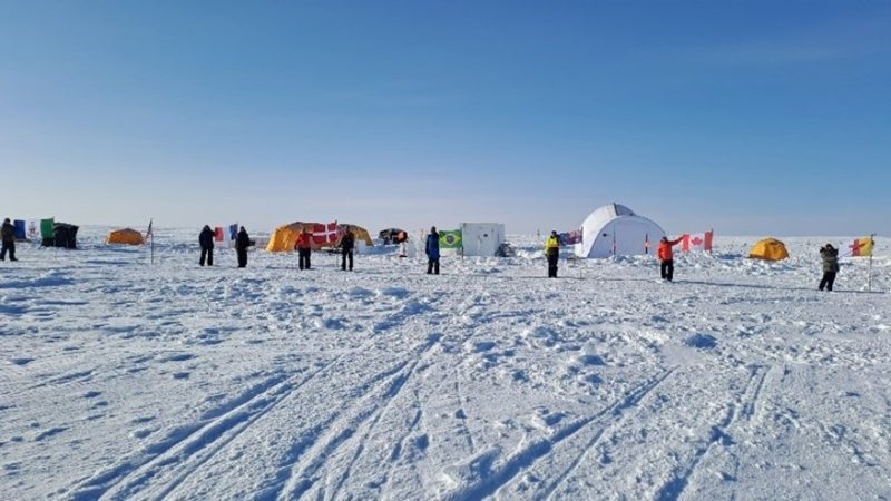 A series of tents and people set up along the international flag line in the Arctic climate.